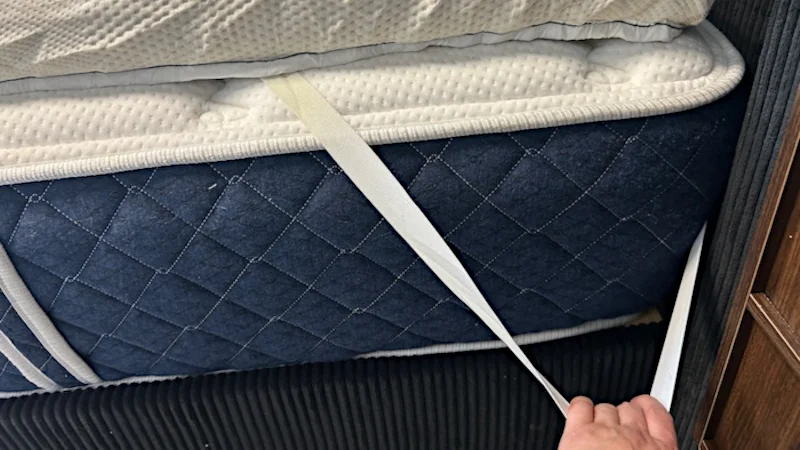Our tester stretches out the corner strap from a Saatva Graphite Memory Foam Mattress Topper