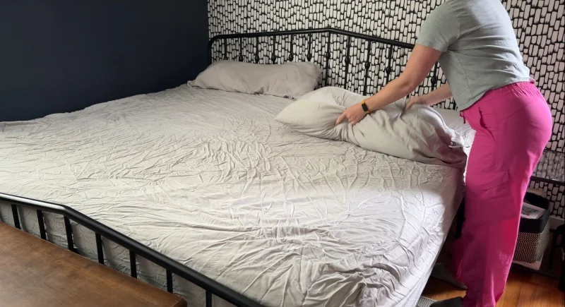 Our tester fluffs a pillow while making a bed with a Quince Bamboo Sheet Set