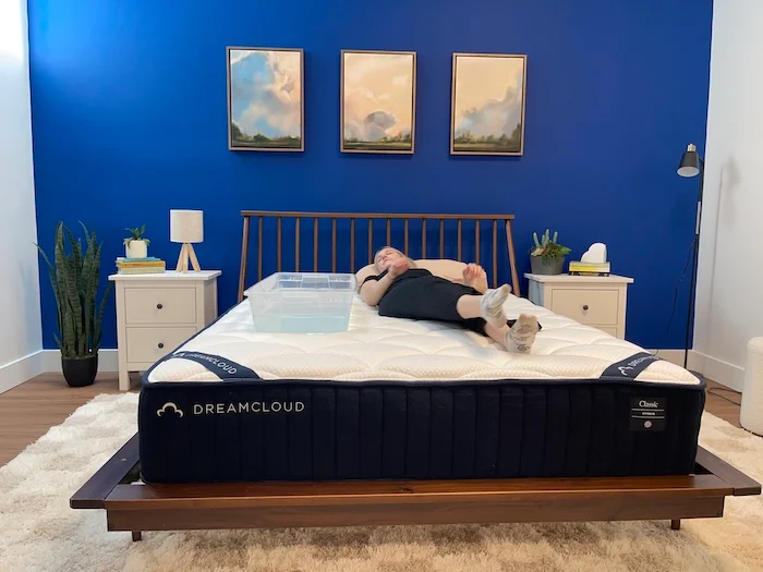 A woman lying on the DreamCloud mattress next to a plastic bin full of water.