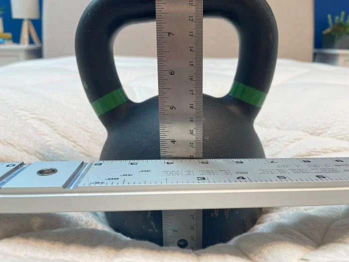 A kettlebell sitting on an Avocado Luxury Organic mattress. A steel ruler is next to it, measuring the sinkage.