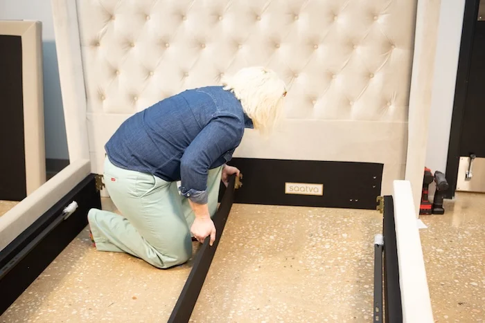 A woman crouching inside the Saatva Amalfi bed frame while the top section is lifted up.