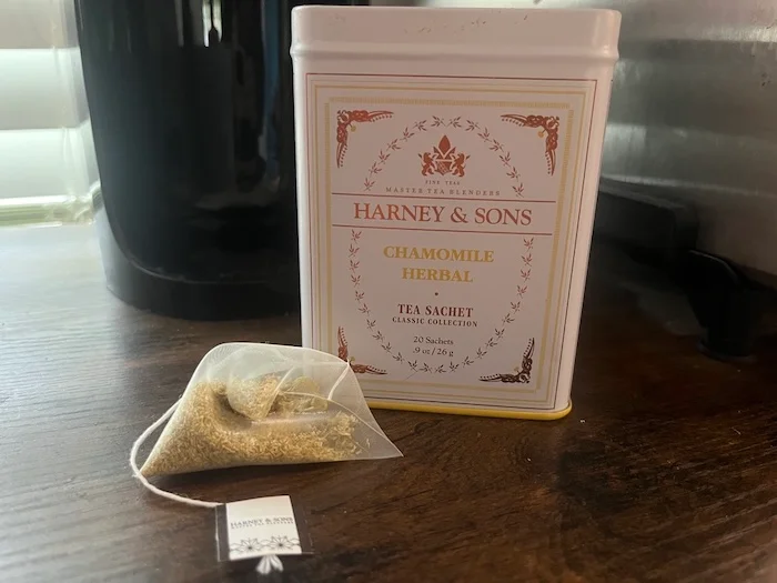 A tea bag rests next to a tin of Harney & Sons Tea.