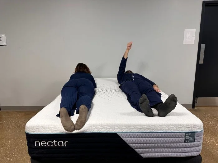 A man on the Nectar Premier mattress raises his arm to indicate felt movement from the woman across the bed