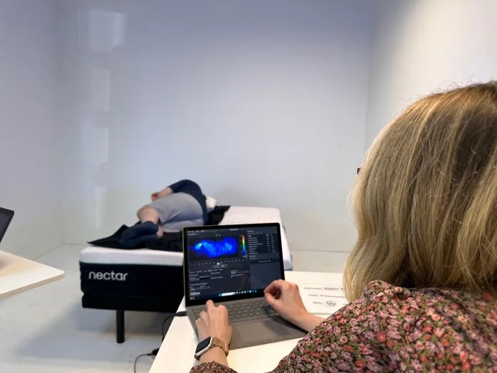 A woman types on her laptop while looking at pressure readings from the heavyweight tester on the Nectar Premier mattress