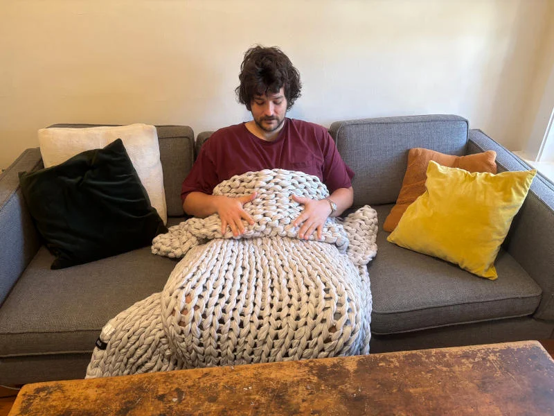 Our product tester sits on couch evaluating the Silk & Snow Handknitted Weighted Blanket
