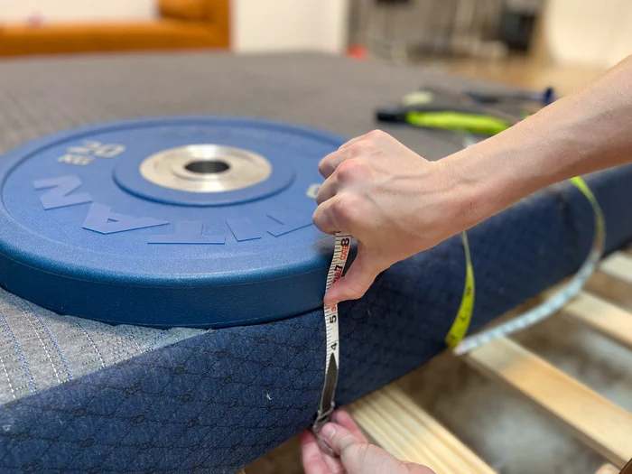 A weight resting on the edge of the BB Kids mattress. One of our testers is measuring the sinkage to test the bed's edge support.