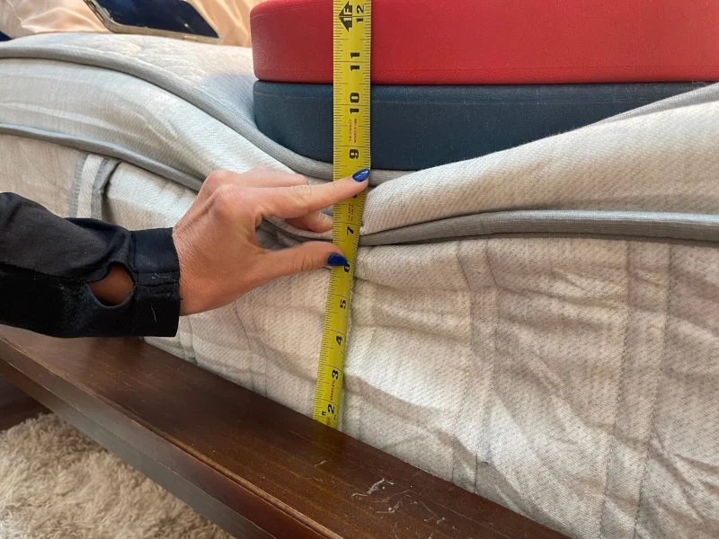 Our tester measures the compression of weight plates to assess edge support on a Leesa Plus Hybrid mattress.