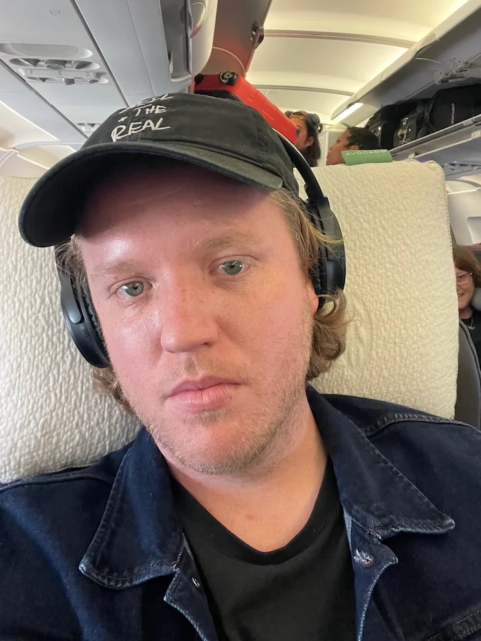 A man sitting in an airplane seat with the Avocado Mini Molded Latex Pillow behind his neck.