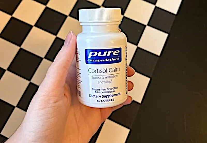 A hand holds a bottle of Pure Encapsulations Cortisol Calm