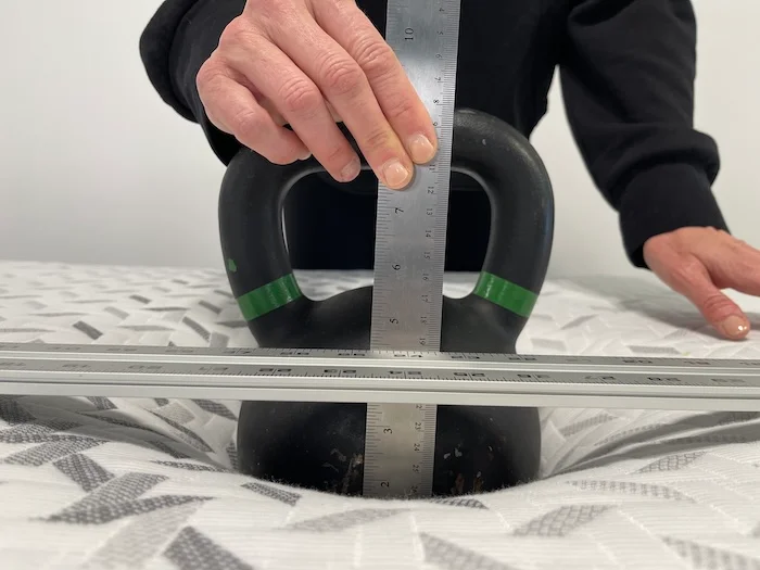 A kettlebell sitting on top of the Nectar. Someone is using a ruler to measure its sinkage.