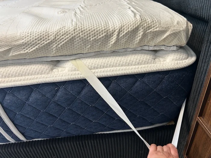 Our tester stretches out the corner strap from a Saatva Graphite Memory Foam Mattress Topper