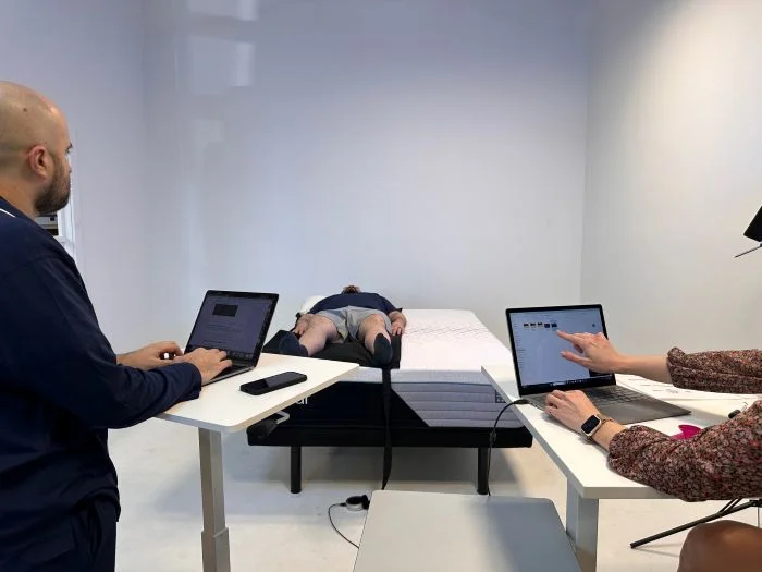 Two testers consult laptops as a man lies on a pressure mat on the Nectar Premier mattress