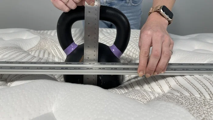 A kettlebell resting on the Nolah Evolution mattress, with one of our testers measuring its sinkage.