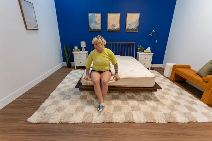 A woman sits on the edge of the foot of the Zenhaven mattress
