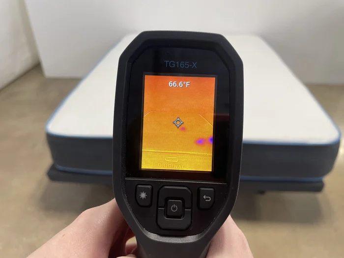 A closeup of someone pointing a thermal gun at the Bear Original mattress to read its temperature. The screen says 66.6 degrees.