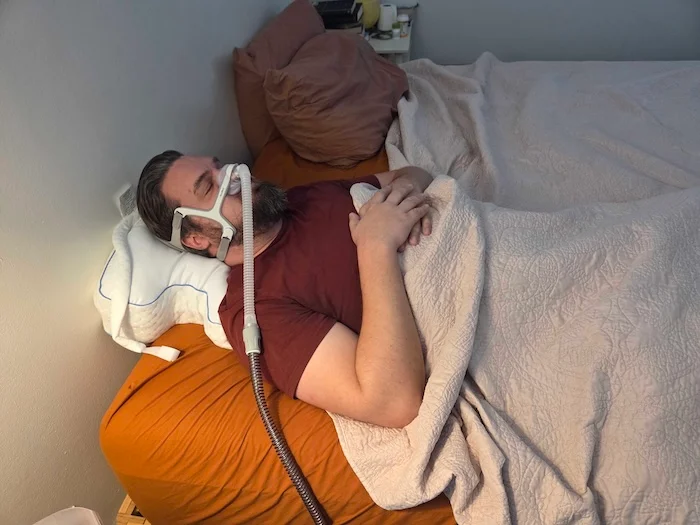 A man sleeping on his back on the Contour pillow. He's wearing a sleep apnea mask as he dozes.