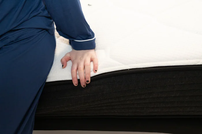 A woman sitting on the edge of the Plank Firm mattress and pressing into its layers to test its edge support.