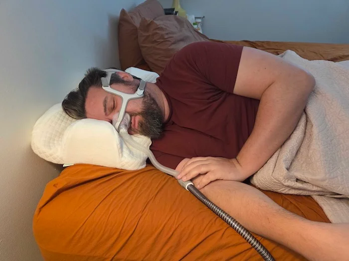 A man sleeping on his side on the Endurimed pillow. He's wearing a sleep apnea mask as he dozes.