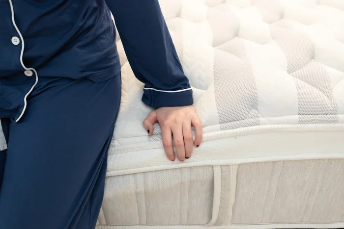 A closeup of a woman sitting on the edge of the Leesa Sapira Chill Hybrid mattress and pressing into its layers.