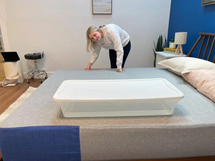 A woman looking at a bin full of water on top of a Casper The One mattress.