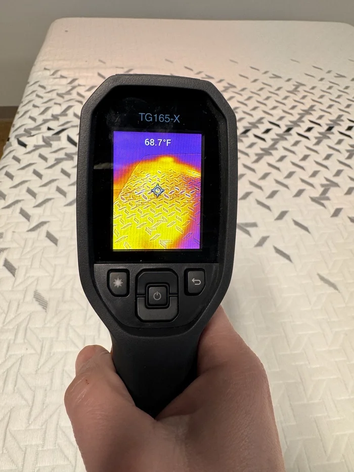 A closeup of someone's hand aiming a thermal gun at the Nectar Luxe Hybrid mattress and measuring its temperature, which reads 68.7 degrees.