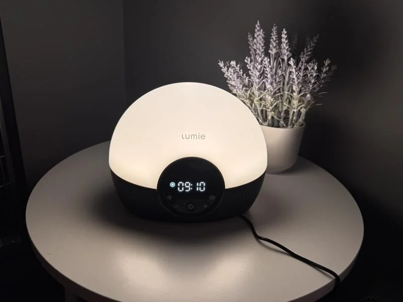 A Lumie Bodyclock Glow 150 on a table next to flowers while glowing white