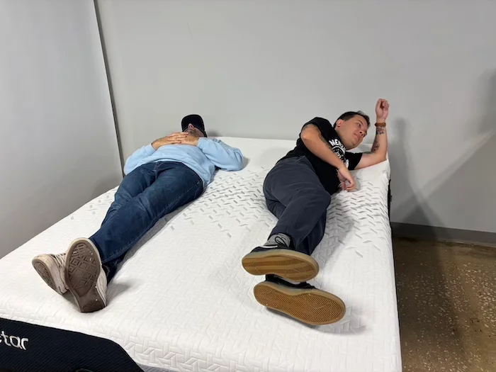 Two men lying on a Nectar Premier Memory Foam mattress. One of them is rolling over to test the bed's motion isolation.