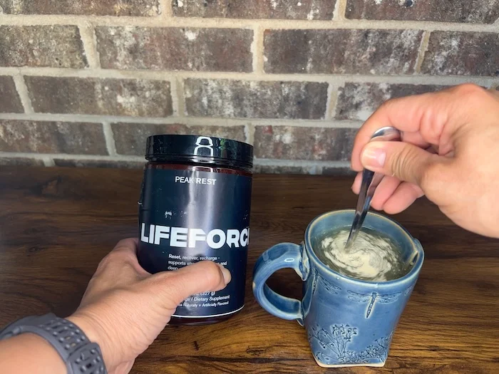 A person holds a container of Lifeforce Peak Rest sleep aid while mixing some in a cup.