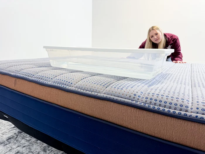 A woman looking at a plastic bin full of water on top of a mattress.