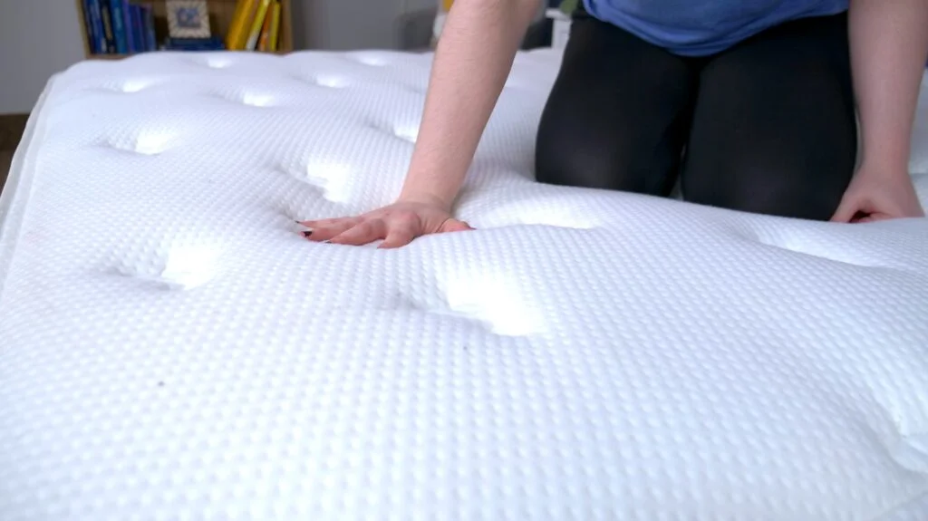 A woman kneeling on the Brooklyn Bedding Signature Hybrid mattress and pressing into its cover.