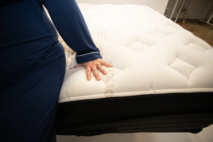 A woman sitting on the edge of the Nolah Evolution mattress and pressing into its layers.